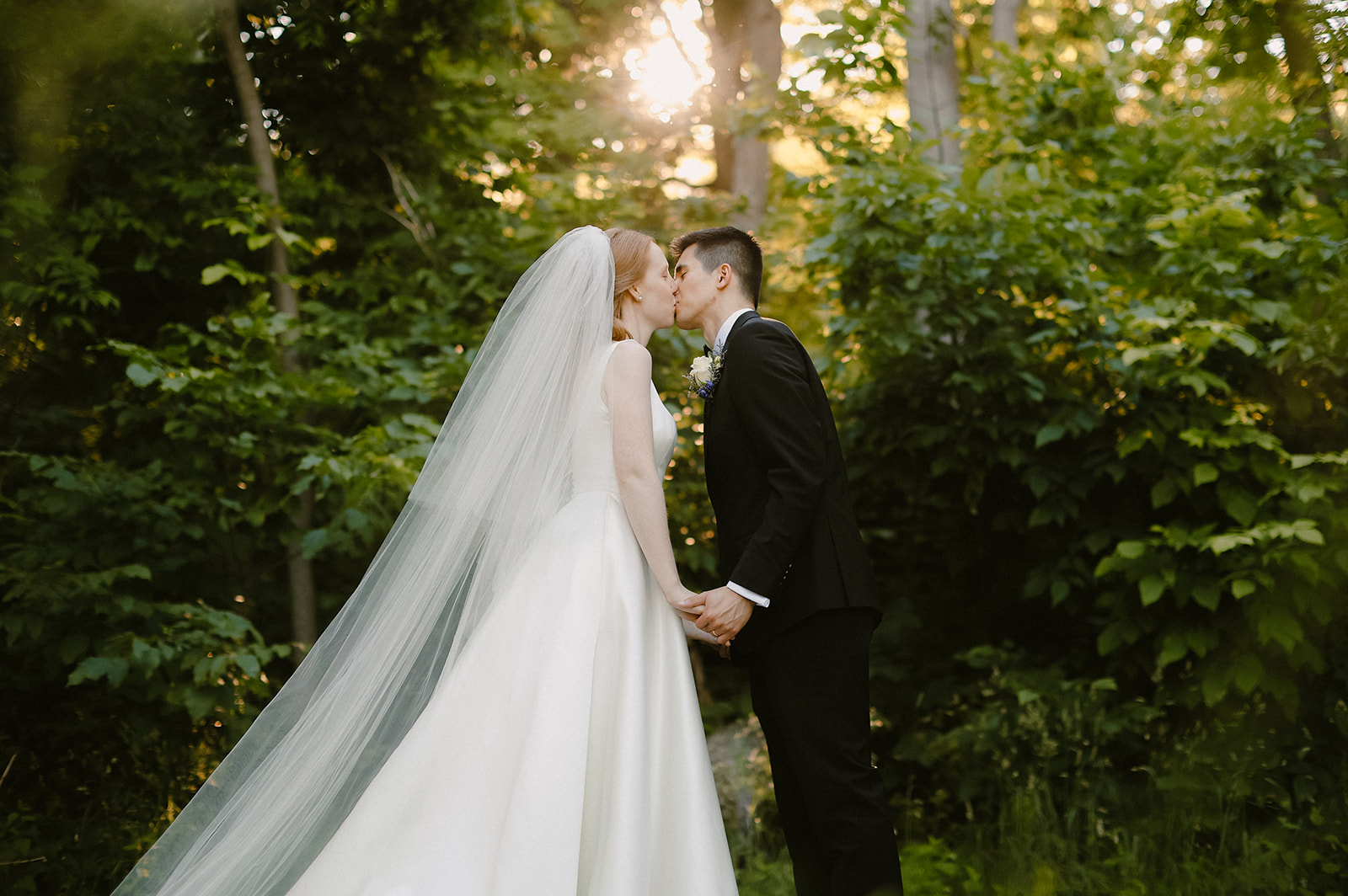 Bride and Groom kiss with green foliage in background.