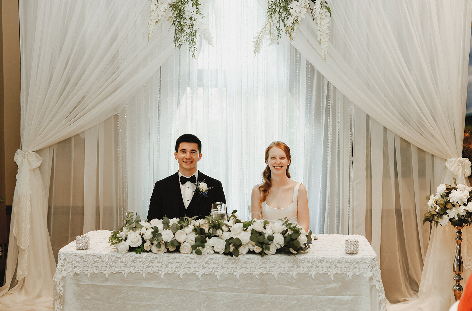 Bride and Groom seated at table smiling. 