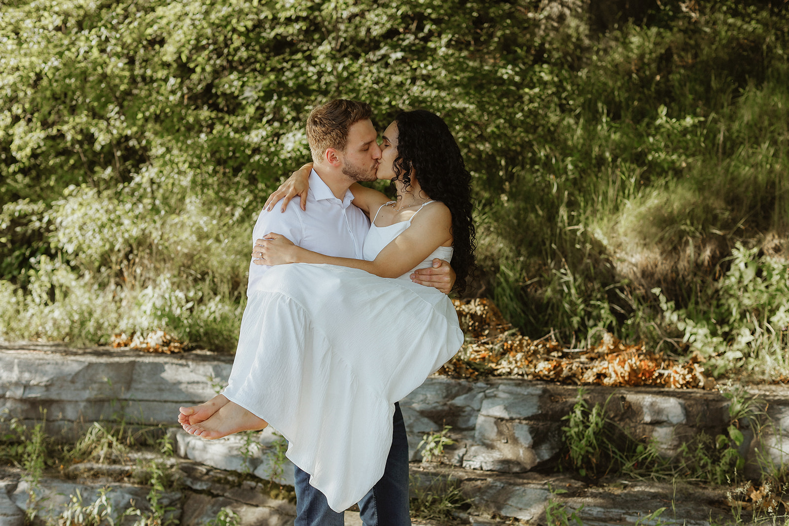 Man holds woman in arms and shares a kiss. Engagement Photo.