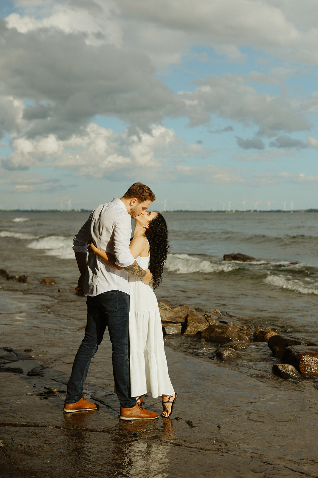 Couple kisses with sky and Lake Ontario in background
