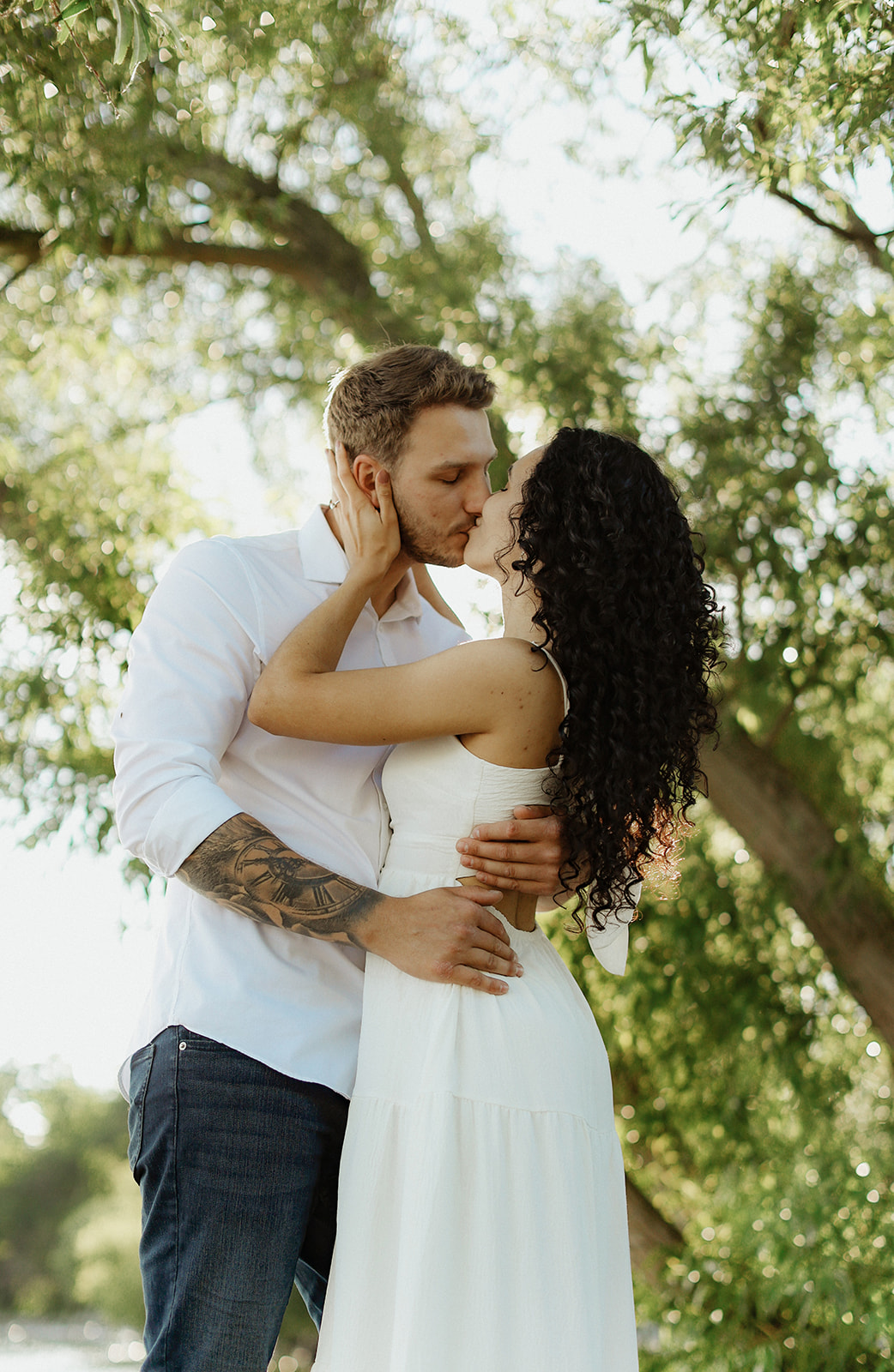 Man and woman kiss under foliage. Engagement Photo