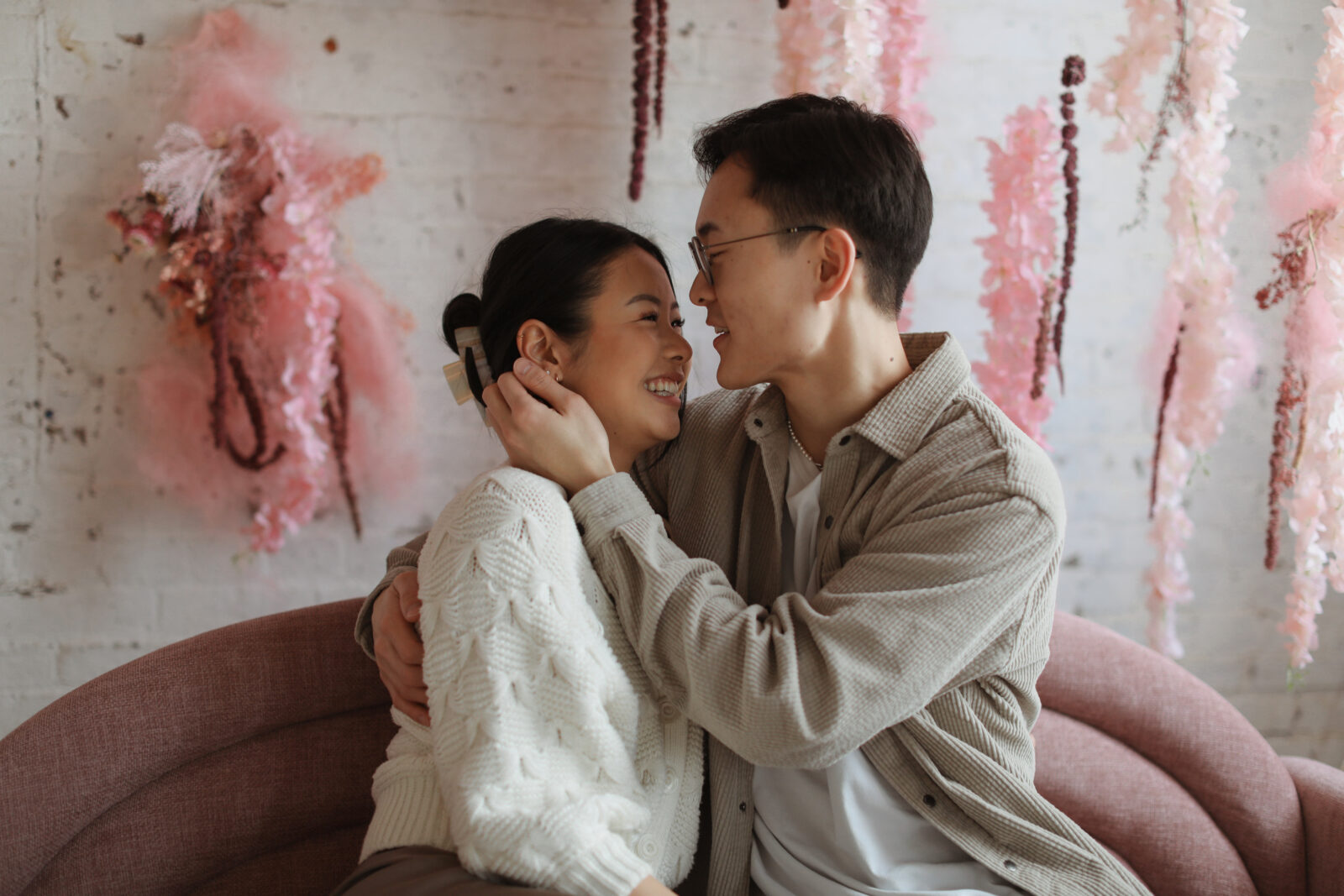 Couple staring into each others eyes. Background white brick with pink flowers