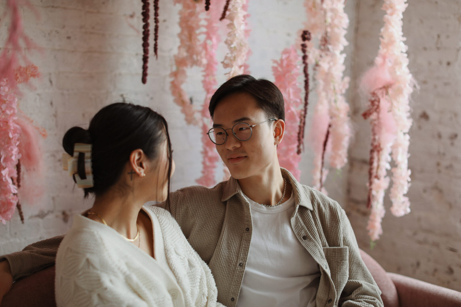 Couple staring into each others eyes. Background white brick with pink flowers