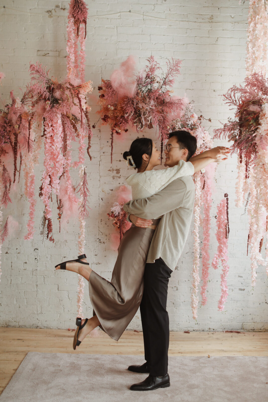 Couple staring into each others eyes. Background white brick with pink flowers