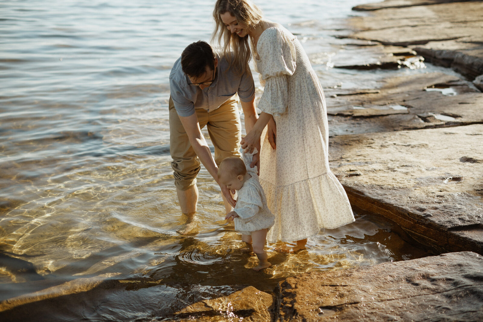 Mom and dad wade into water with baby. Family photography sessions - Kingston Ontario