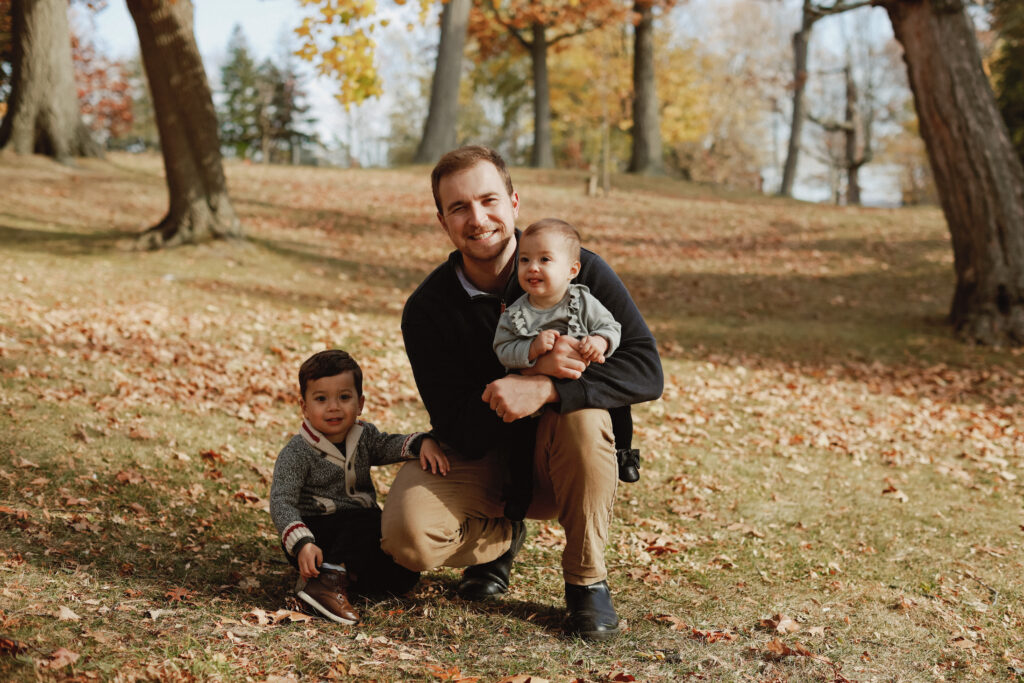 Father holds baby while son sits net to them with hand on knee. 