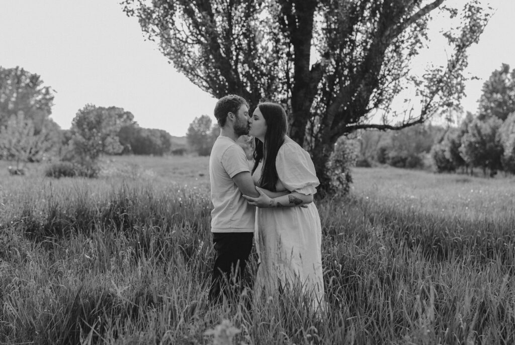 black and white photo of couple kissing in field. 