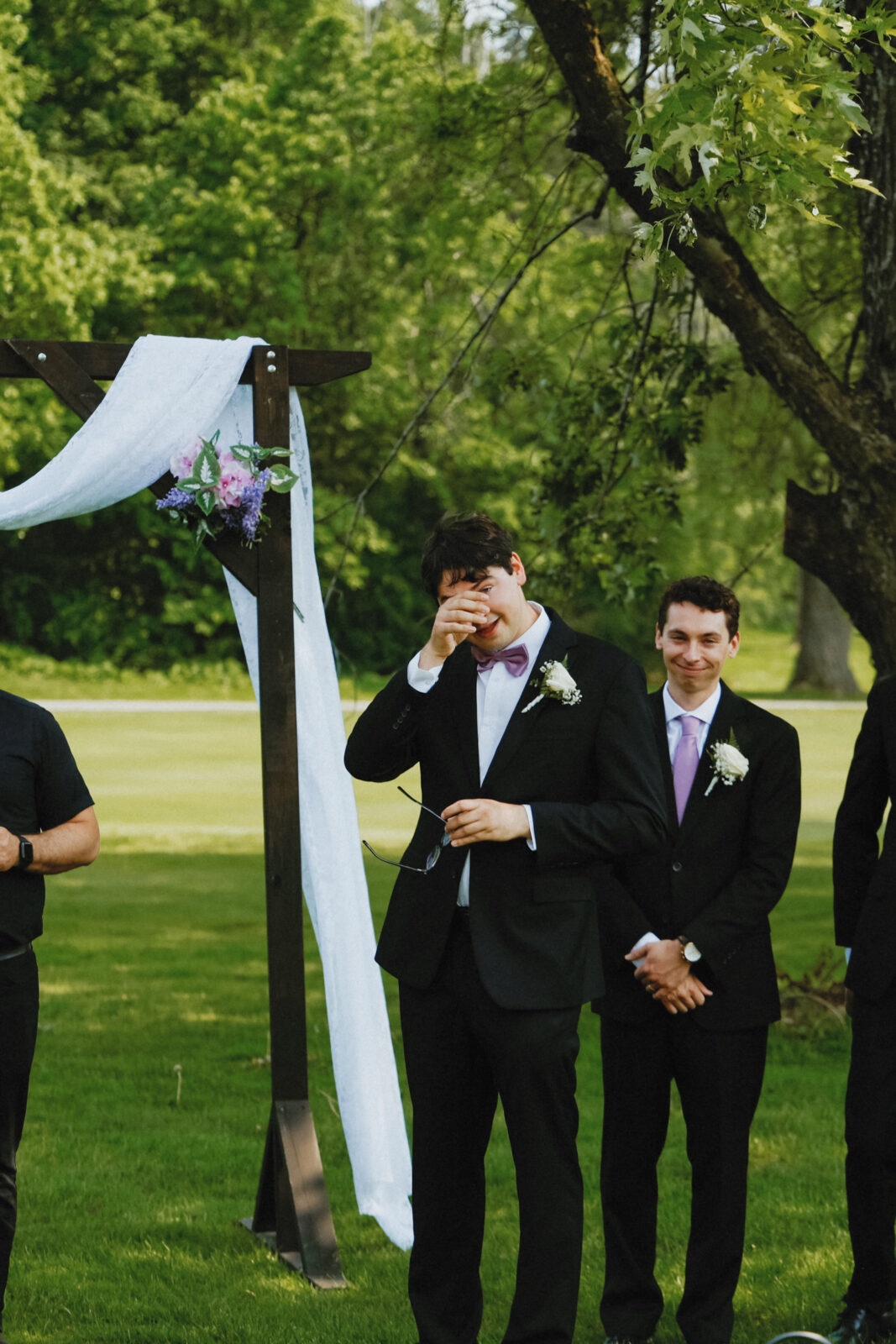 Groom wipes tears away while watching the bride walk down the aisle