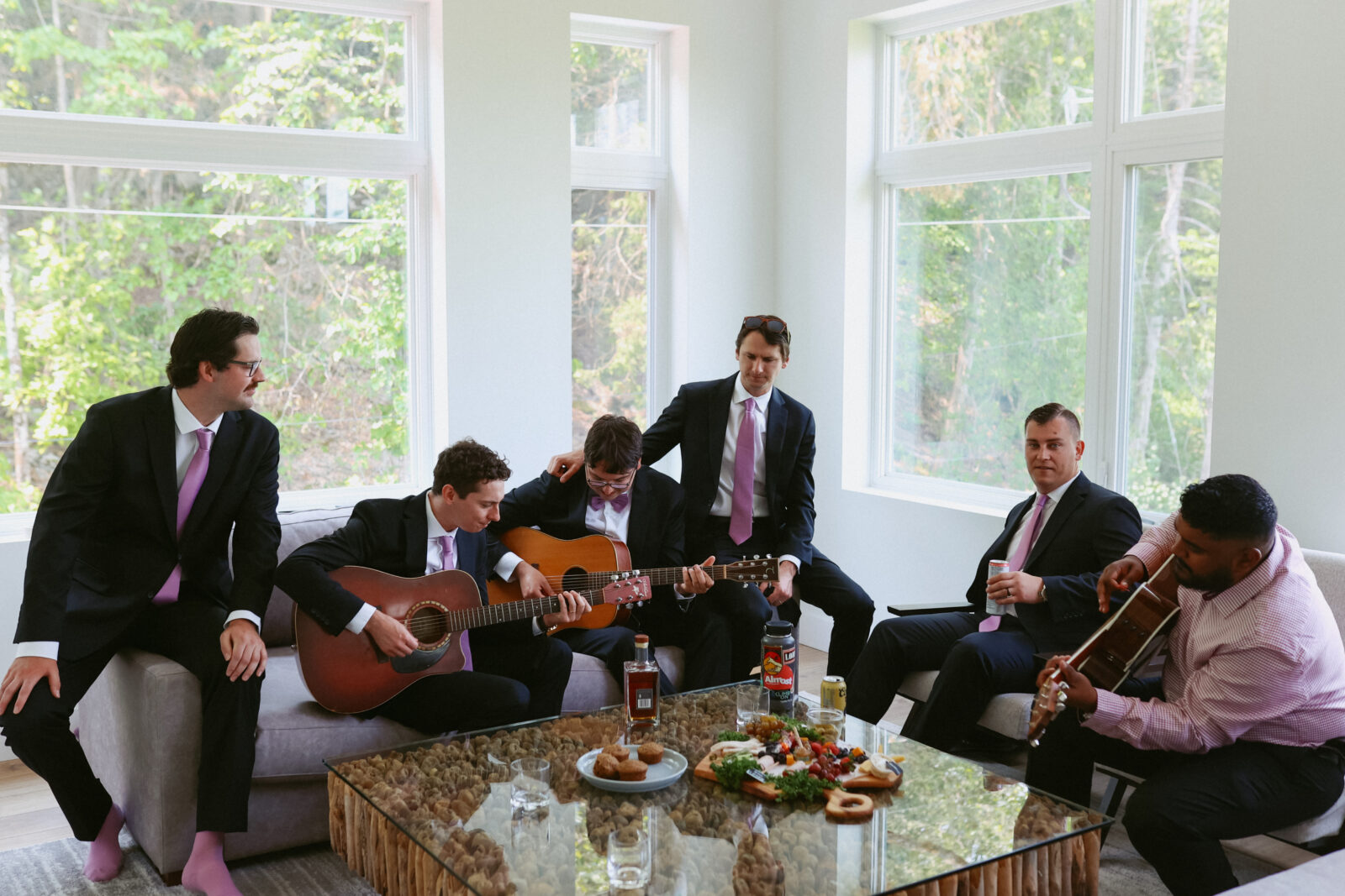 Groomsmen play guitar together on couch while getting ready for the wedding.