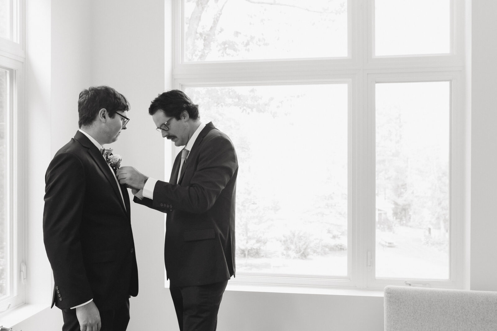 black and white photo of groom getting ready for his wedding. Friend is placing flowers in lapel.