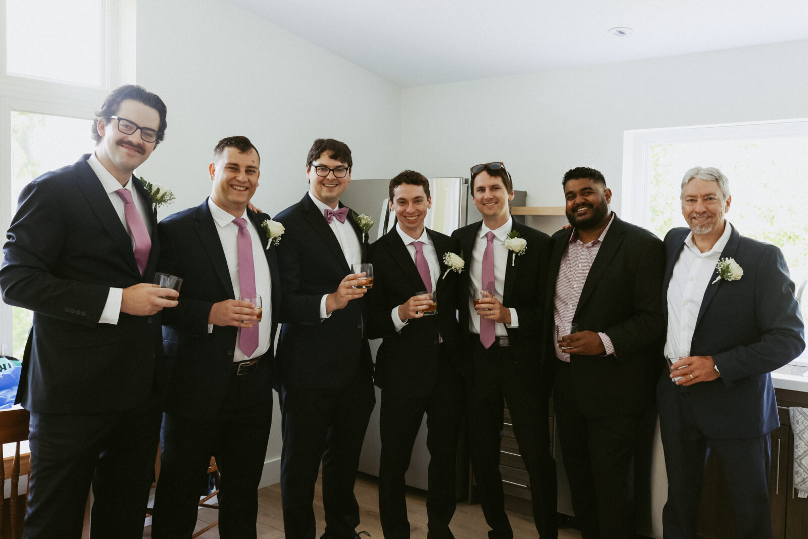 Groomsmen pose for a photo with glasses in hand. 