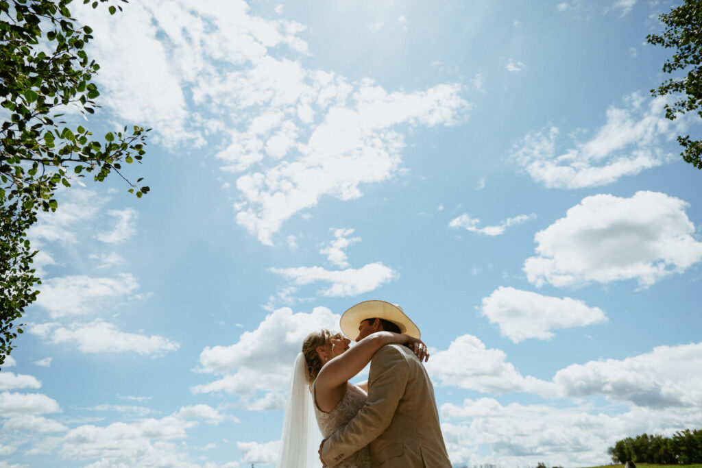 Blue summer sky with clouds. Bride and Groom hug in forefront
