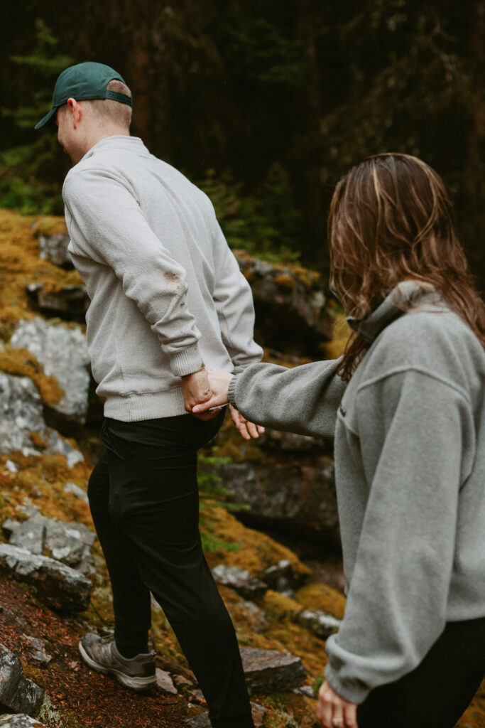 couple walks in woods holding hands