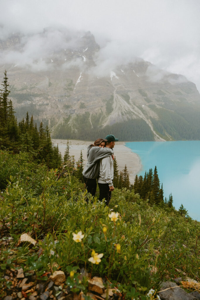 Couple hugs with crystal blue lake in the background. 