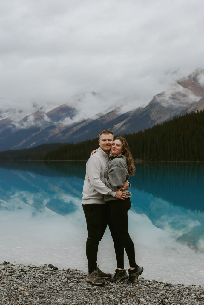 Couple hugs on a rock shoreline in Alberta.