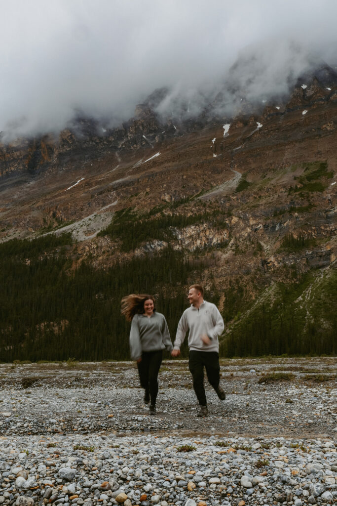 Couple runs towards camera on a rock beach in Alberta.