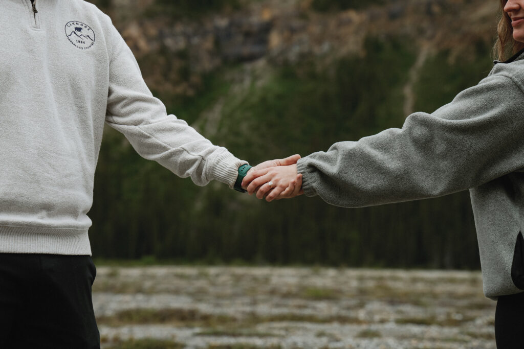 Couple holds hands on beach showcasing a engagement ring.