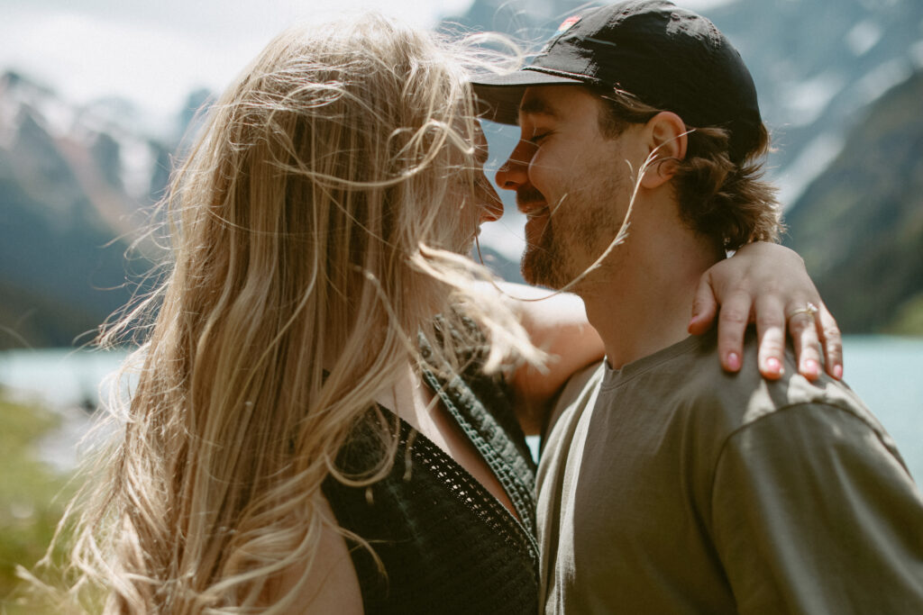 Couple kisses during engagement photoshoot with mountains and a lake in the background