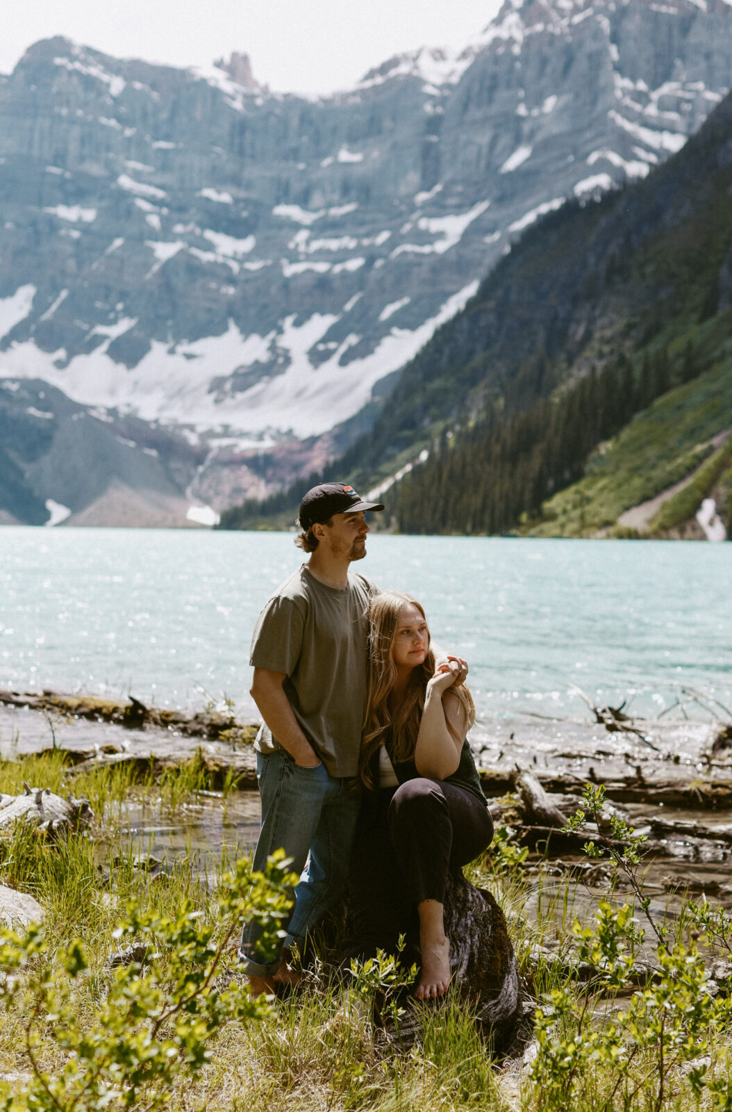Couple lean on each other during a engagement photoshoot with mountains and a lake in the background