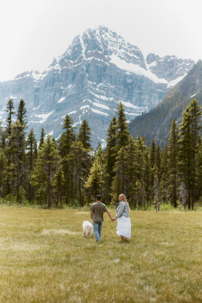 Couple holds hands and walks towards mountains in the background