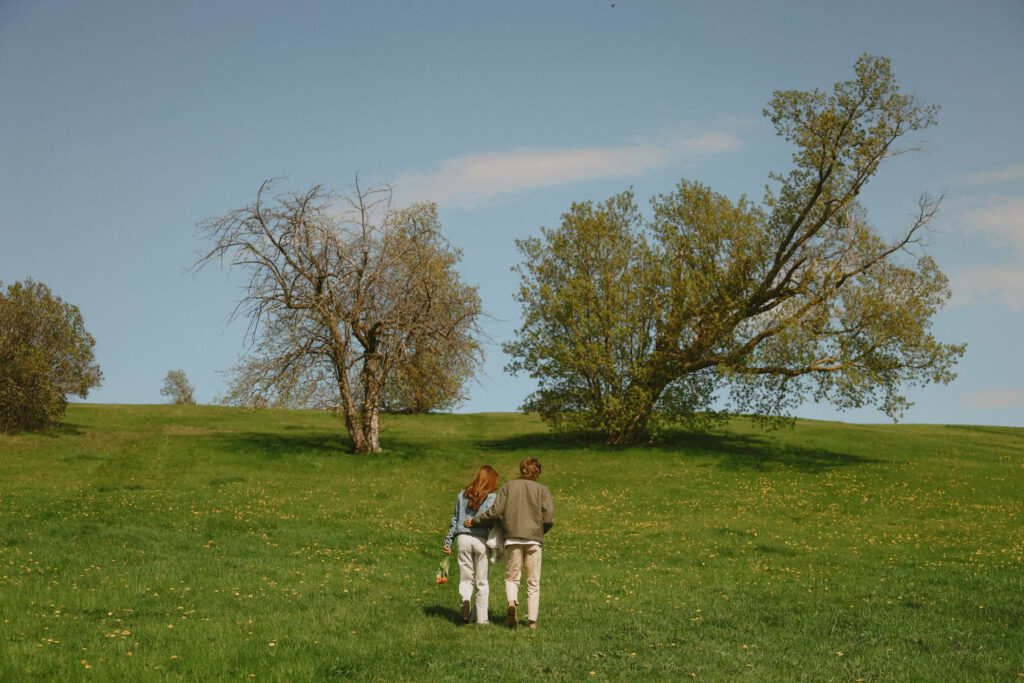 couple walks up grass hill. 