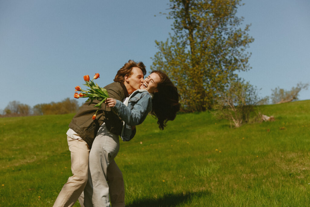 Man kisses woman with tulips in her hand. Woman is laughing. 