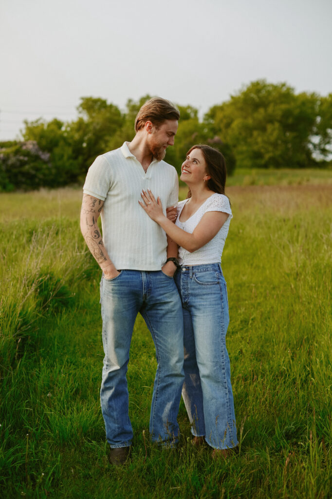 Couple stands in field smiling at each other. Engagement photography.