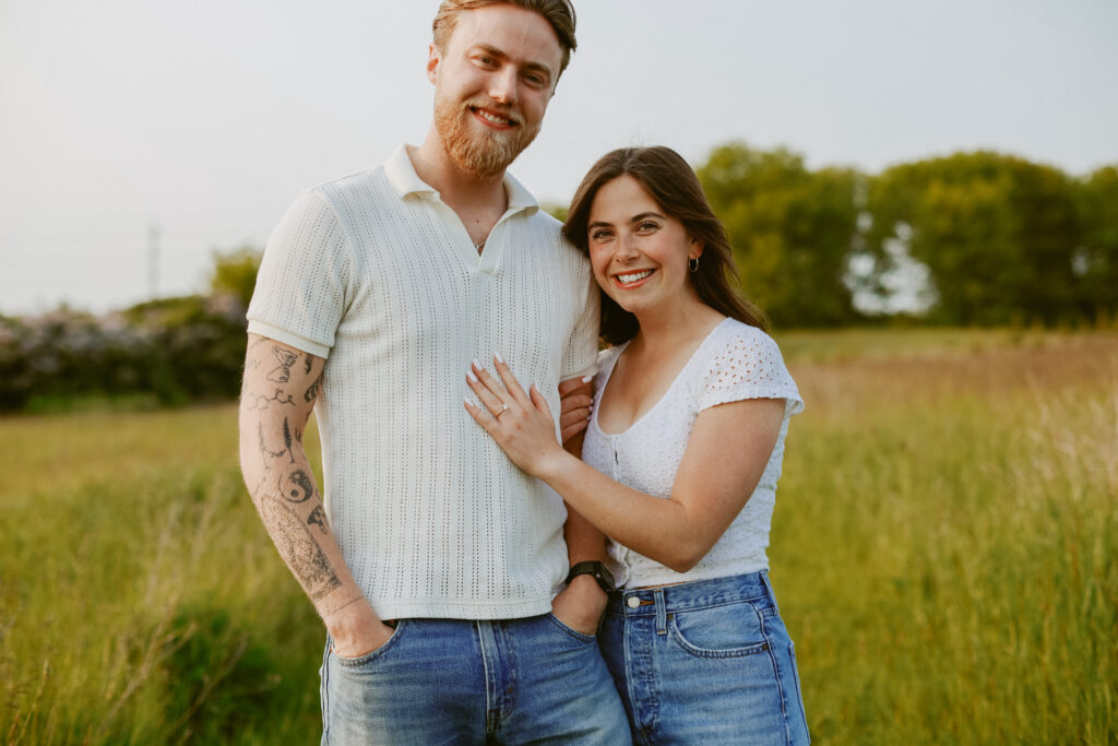 Couple stand in field smiling. Engagement photography 