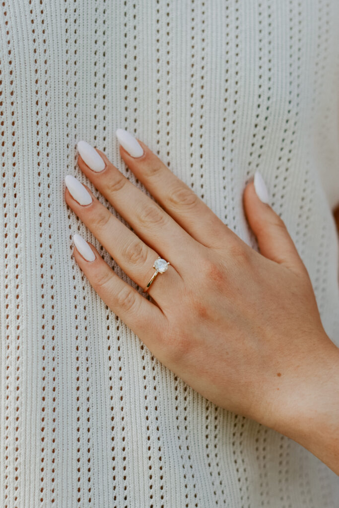 Woman's hand rest against white background with a close up on a gold engagement ring. 